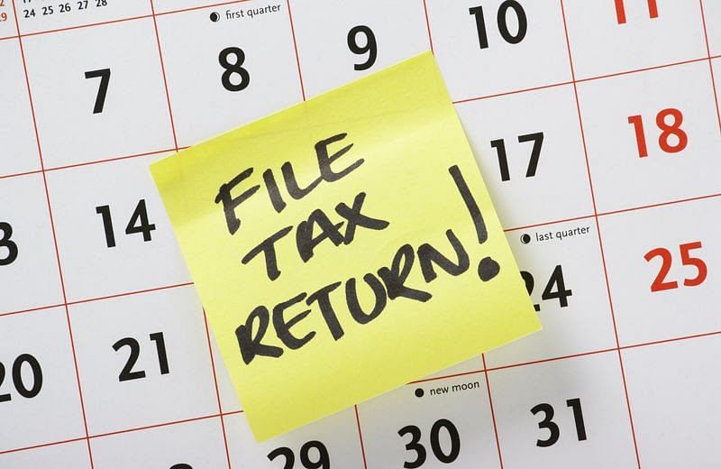 Handwritten reminder to File Tax Return on a yellow post it note stuck to a calendar background