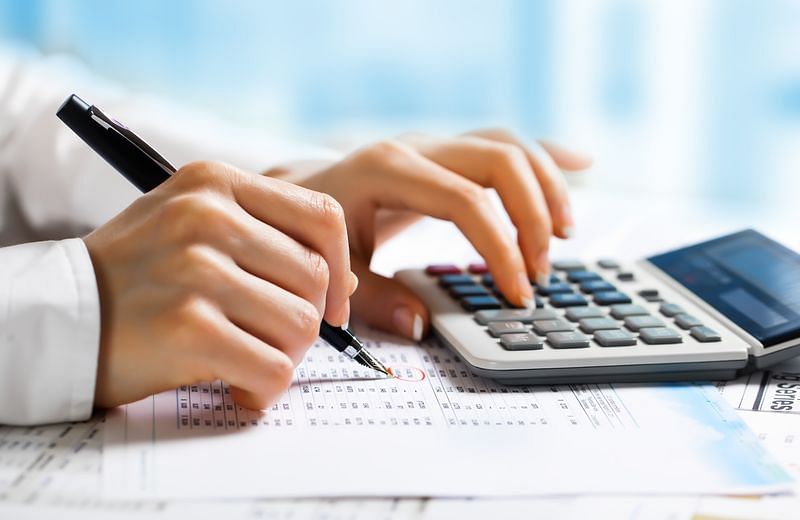 federal income tax rate - A woman encircling amounts on a financial report while using a calculator