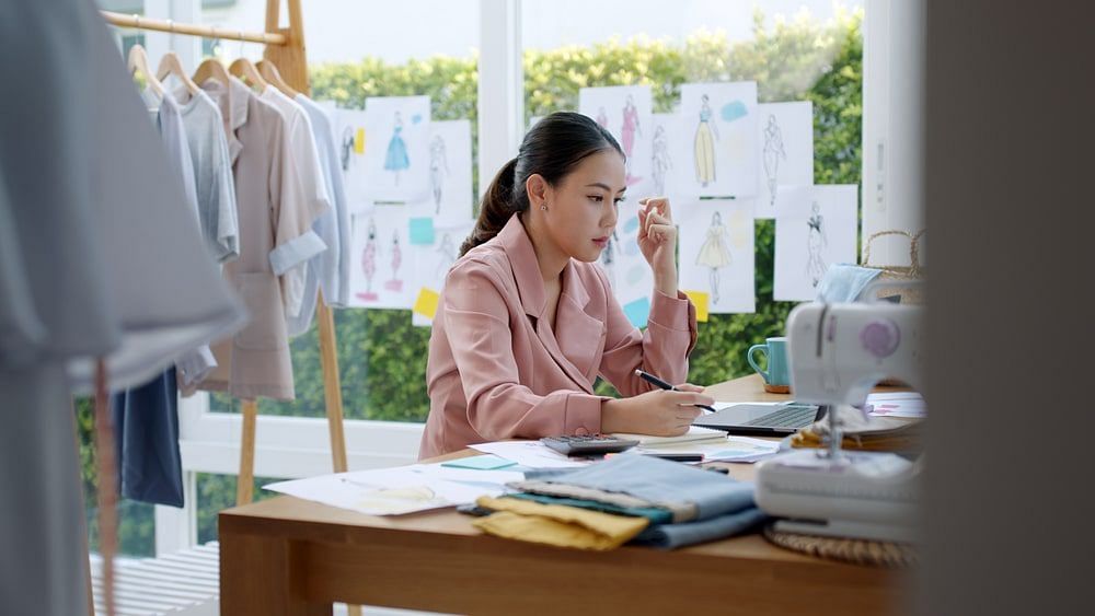 A small business owner filing for sales tax surrounded by her clothing products and sketches 