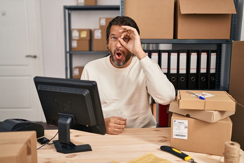 Ecommerce bookkeeping - A man sitting behind a wooden desk makes a circle figure around his eye with his fingers
