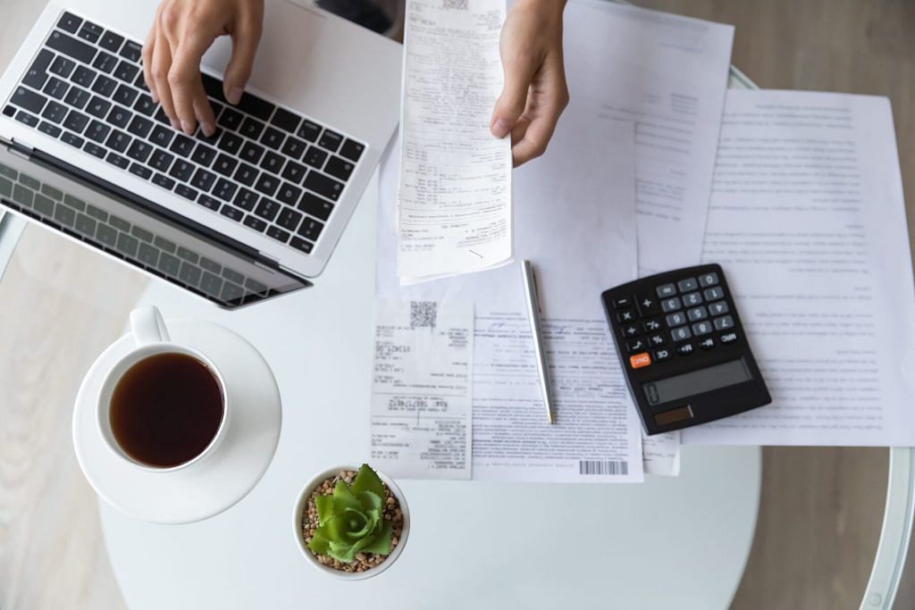 ecommerce bookkeeping - Above top view close up young woman holding utility bills or receipt, managing monthly expenses with e-banking application on computer, professional accountant or bookkeeper doing paperwork indoors