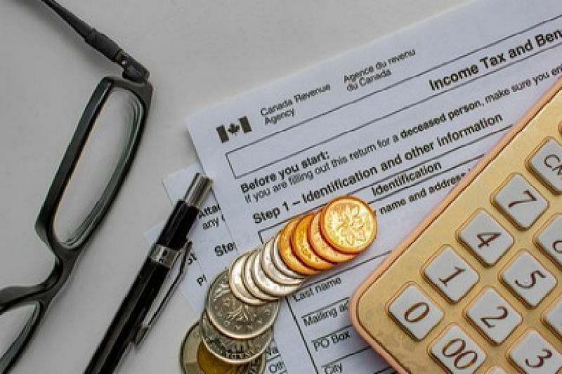 Sales tax in canada - Spare change, a calculator, a pen, glasses, and a form for Income Tax for the Canada Revenue Agency.