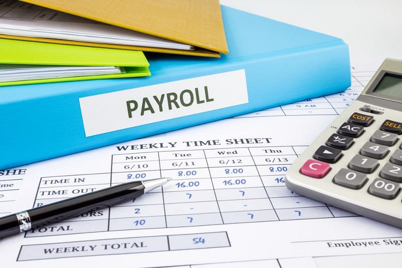 payroll book with weekly time sheets, a pen, and a calculator on a work desk