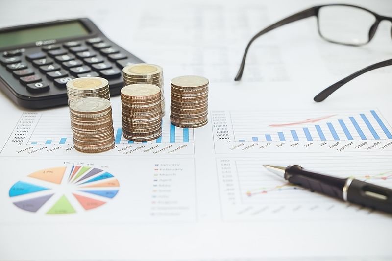 January to December accounting charts printed on a paper surrounded by an eyeglass, pen, calculator, and coins