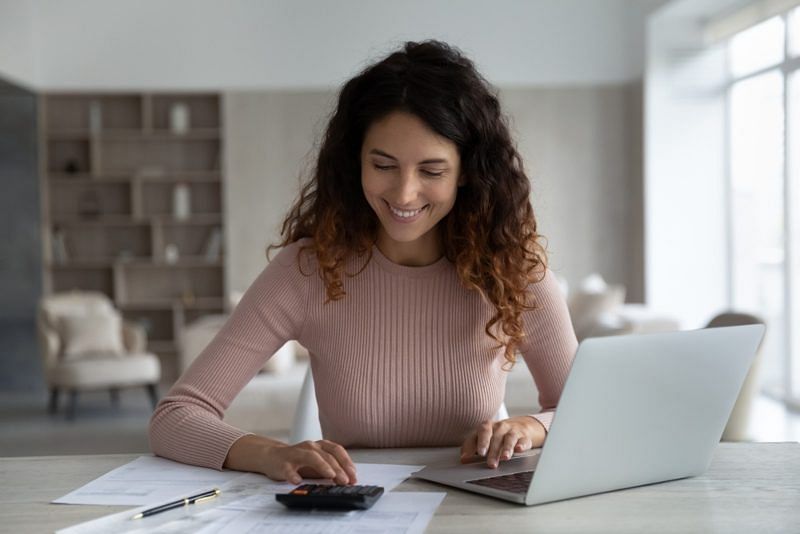 shot of a bookkeeper smiling while computing with a calculator and their laptop open