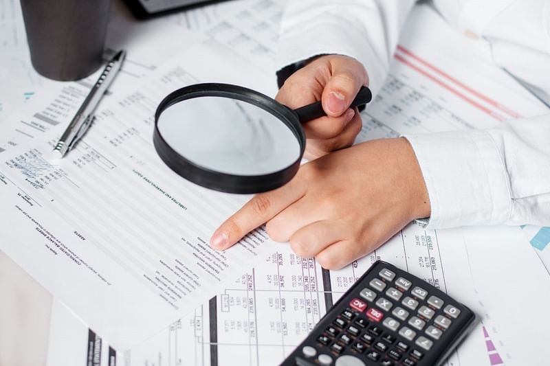 a man looking at financial statements on a table surrounded by a glass, a pen, and a calculator using a magnifying glass