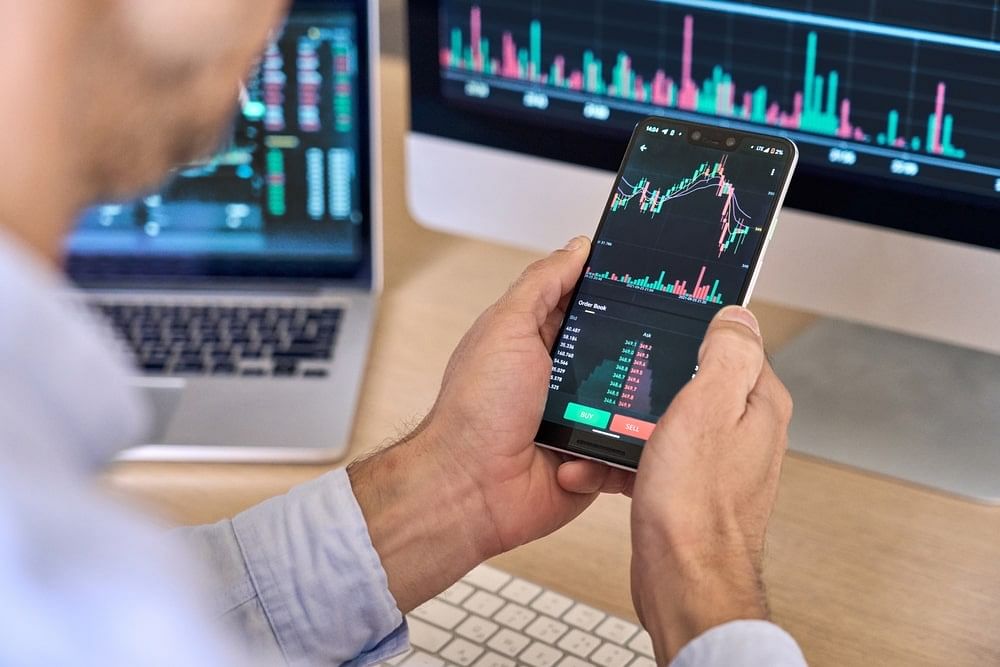 A pair of male hands holding a smartphone that projects a line graph of trends on its screen.