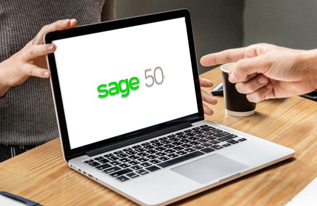a hand pointing out an opened laptop with sage 50 software on the screen