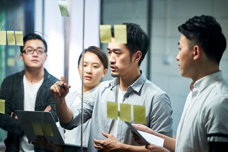 A team of professionals having a brainstorming session by posting notes on a clear glass.